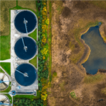 Aerial view of an industrial facility with three large circular tanks next to a natural wetland area, showcasing the contrast between developed and natural landscapes.